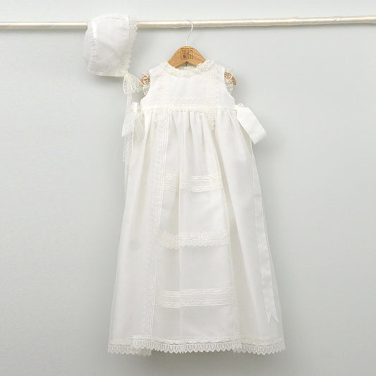 Faldón de bautizo de organza natural con encaje bordado central, remates de puntilla de topos y lazos laterales de cinta de ángel, estilo clasico