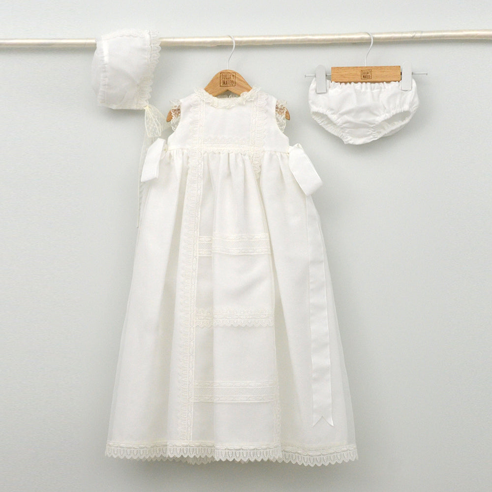 Faldón de bautizo de organza natural con encaje bordado central, remates de puntilla de topos y lazos laterales de cinta de ángel, estilo clasico