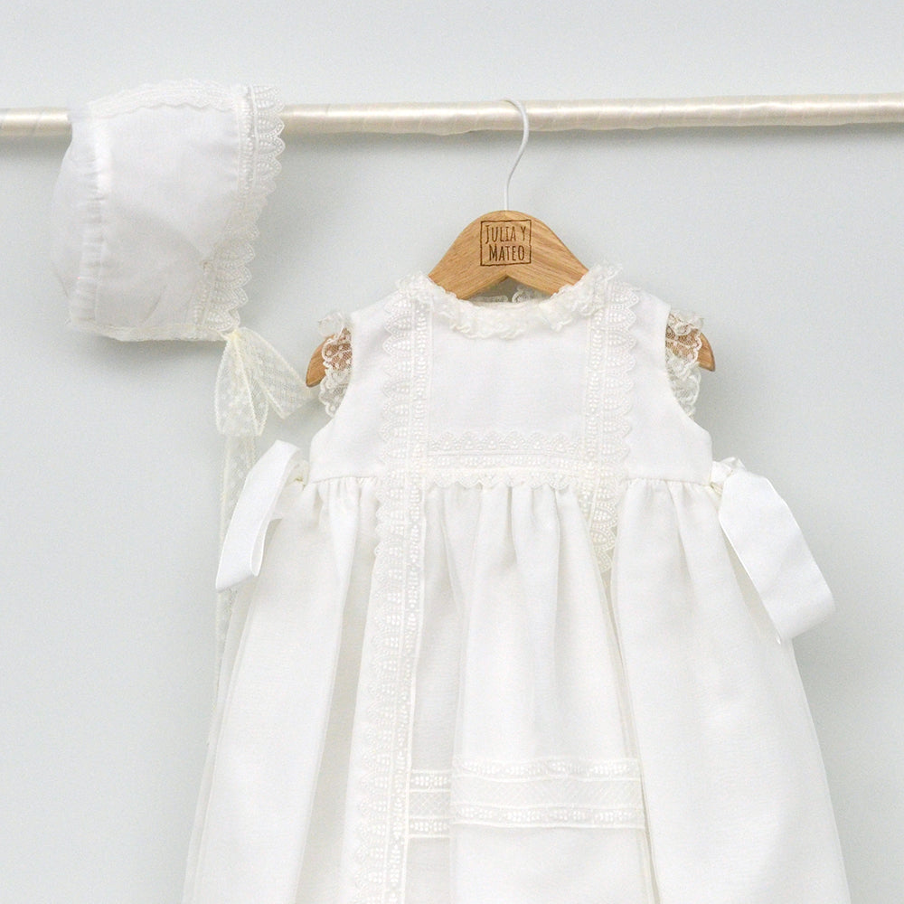 Faldón de bautizo de organza natural con encaje bordado central, remates de puntilla de topos y lazos laterales de cinta de ángel, estilo clasico