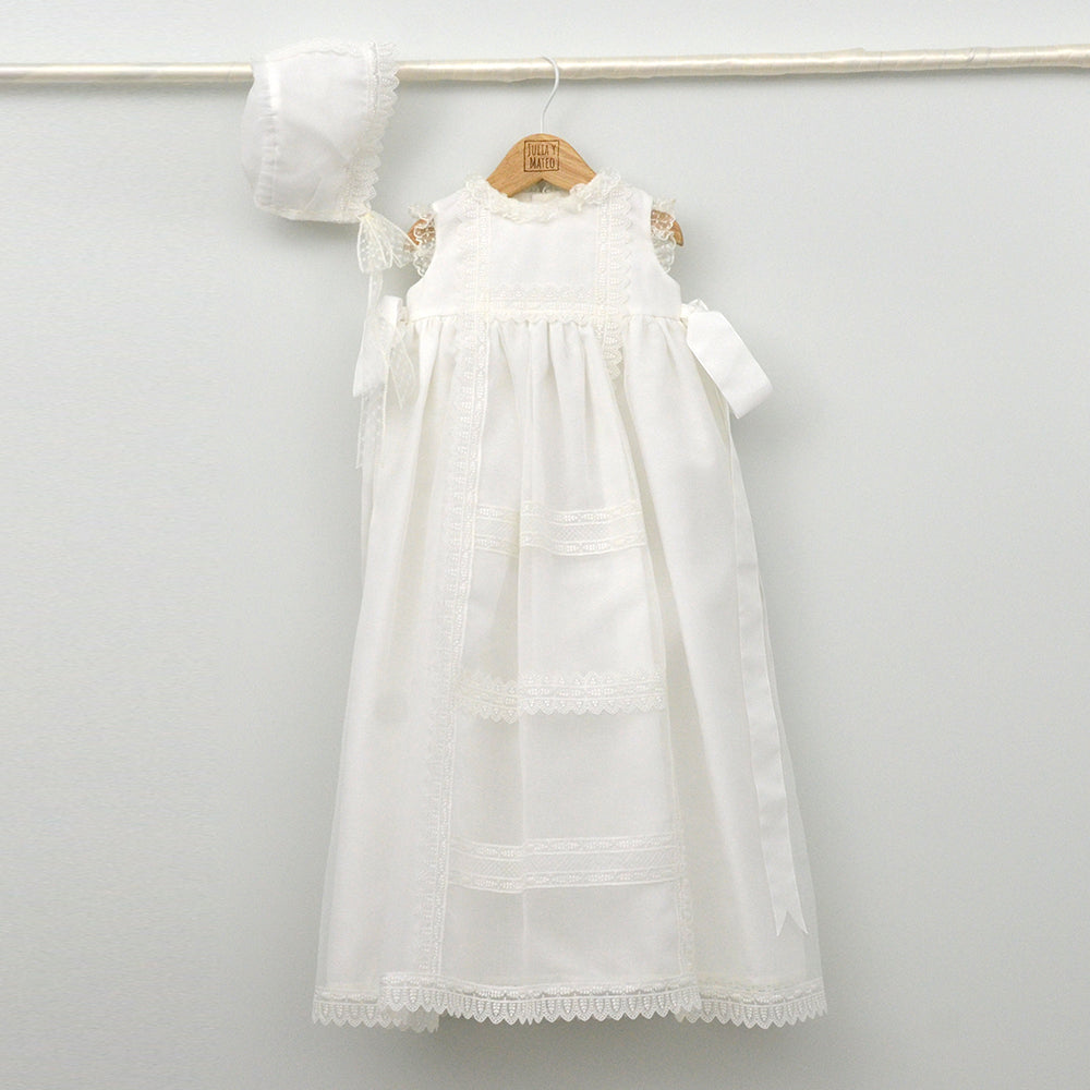 Faldón de bautizo de organza natural con encaje bordado central, remates de puntilla de topos y lazos laterales de cinta de ángel, estilo clasico
