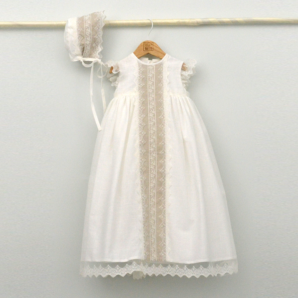 Conjunto de bautizo de la marca Julia y Mateo compuesto por un faldón largo en color blanco roto con franja central de encaje beige, capota a juego y cubrepañal, Primavera 2026