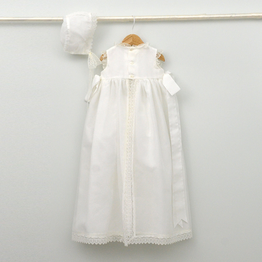 Faldón de bautizo de organza natural con encaje bordado central, remates de puntilla de topos y lazos laterales de cinta de ángel, estilo clasico